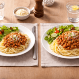 2 tallrikar med pasta, köttfärssås och sallad där 1 tallrik har mer mat än den andra.